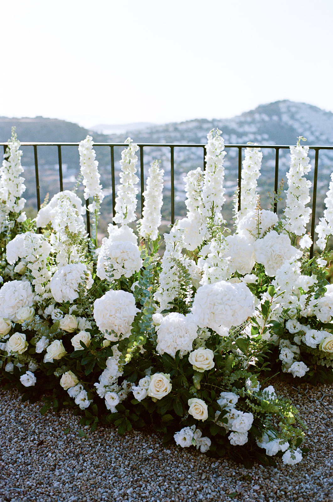 Kate & Can - Yalikavak, Bodrum, Türkiye Wedding | Meredith Lord Photography www.meredithlord.com - Meredith Lord Photography White floral border with hydrangeas and tall white delphiniums along a black railing against distant hills.