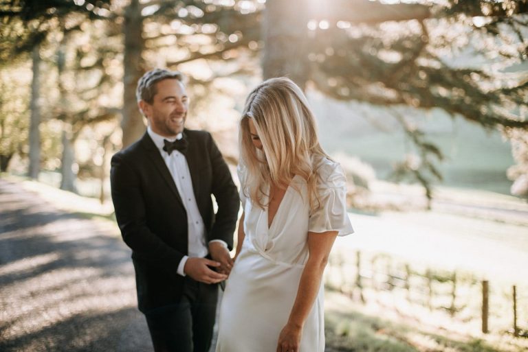 laughing couple in autumn light diffused by trees in wedding dress and tux